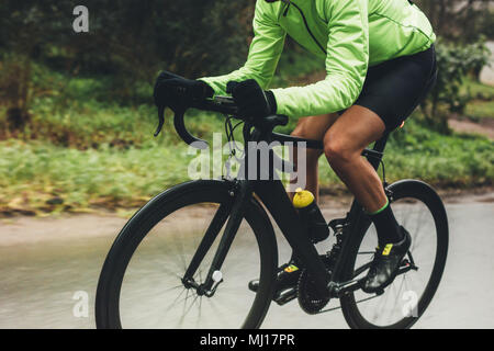 Radprofi Reiten Fahrrad im Freien. Männliche Athlet im Radsport Gang üben auf nasser Straße. 7/8 geschossen. Stockfoto