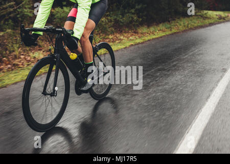 Männliche Athlet im Radsport gang Reiten Fahrrad auf nasser Straße. Niedrige Abschnitt Schuß von Radfahrer Training im Freien an einem regnerischen Tag. Stockfoto