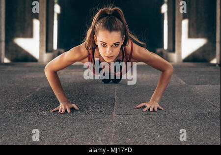 Passen junge Frau tun Push-ups Übungen im Freien. Sportlerin tun core Übungen. Stockfoto