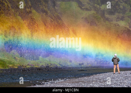 Mann beobachten der Skógafoss Wasserfalls Regenbogen, Skógá Fluss, Island Stockfoto