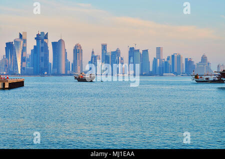 Am Morgen Blick auf Al Dafna viertel Wolkenkratzer in leichten Dunst mit der Dhow Boote und helle blaue Wasser des Persischen Golfs im Vordergrund, Doha, Qa Stockfoto