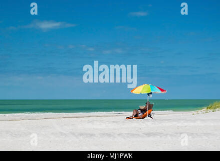 Pärchen, die sich unter einem Sonnenschirm an einem Florida Strand entspannen. Stockfoto