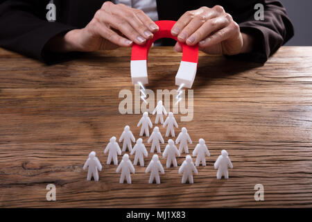 Der Unternehmer Hand zieht menschliche Figuren mit Hufeisen Magnet auf hölzernen Schreibtisch Stockfoto