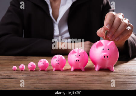 Nahaufnahme der Kaufmann Hand einfügen Münze in Sparschwein über Holz- Schreibtisch Stockfoto