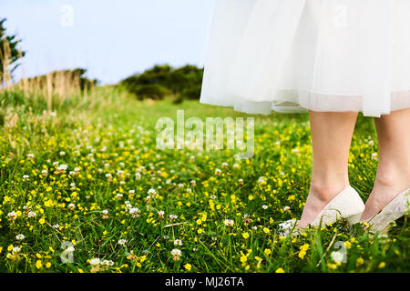 Asiatische Frau tragen weiße geschnürt Brautkleid und weißen Heels an der gelben Blüte Feld auf den Klippen der schönen Insel Jeju entfernt Stockfoto