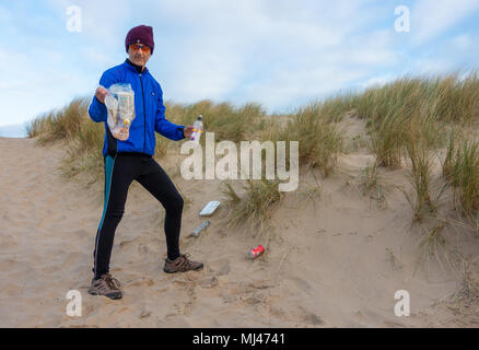 Ein Jogger Plogging (Abholung Wurf beim Joggen) auf seinen Morgen durch Sanddünen. DE Stockfoto