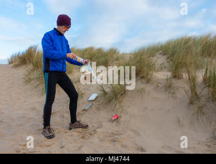 Ein Jogger Plogging (Abholung Wurf beim Joggen) auf seinen Morgen durch Sanddünen. DE Stockfoto