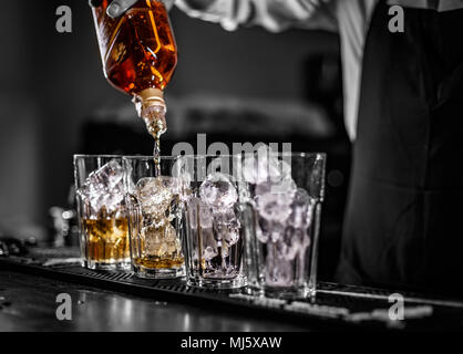 Barkeeper gießen alkoholisches Getränk in die Gläser mit Eiswürfeln auf der Theke Stockfoto