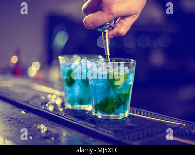 Barkeeper gießt blue Sirup in ein Glas mit Eiswürfeln auf der Theke Stockfoto