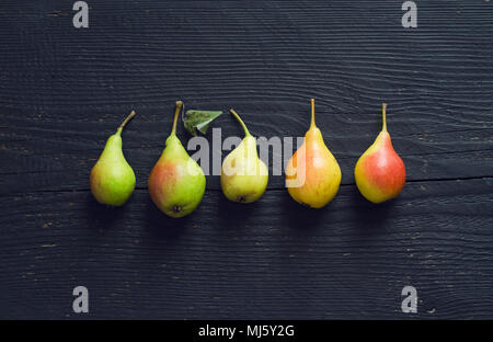 Bunte Birnen in einer Reihe über dunklen Holztisch organisiert, oben anzeigen Stockfoto