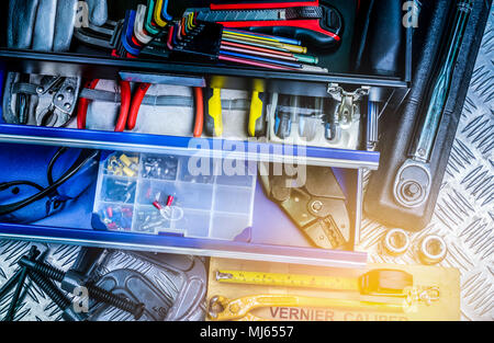 Blick von oben auf die Werkzeuge im Kasten auf karierten Platte Hintergrund in der Werkstatt. Service Tools. Startseite Gebäude und elektrische Werkzeuge. Klempner Handwerkzeuge. Technic Stockfoto