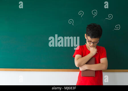 Smart Junge im roten T-Shirt mit dem Denken in der Nähe der Tafel. Bildung und Führung Konzept. Stockfoto