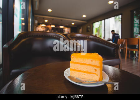 Orange Kuchen auf kleinen weißen Schale mit Löffel am Tisch im Café Stockfoto