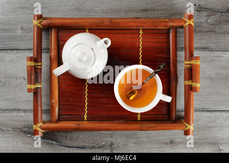 Tabelle Draufsicht auf bambus holz Tablett mit kleinen Keramik Teekanne und Tasse Tee voll Heiß dampfenden schwarzem Tee und silbernen Löffel. Stockfoto