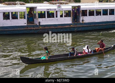 Alappuzha, Kerala/Indien - 15. April 2018: Ein Mann ist Paddeln ein Holzboot mit seiner Familie während einer schnellen Motor angetrieben Pendler Boot ist vorbei. Stockfoto