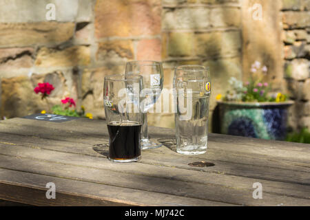 Drei leere oder halb leer Bier- und Weingläser auf einem außerhalb Holz- pub Tabelle in einen Biergarten. Die Gläser sind Marken Guinness, Stowels und fördert Stockfoto