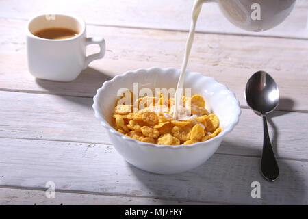 Milch in eine Schüssel leckere Corn Flake Getreide und Kappe mit Espresso gießt. Frühstück am Morgen. Stockfoto