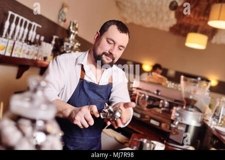 Cute bärtigen barista Mann hält ein Halter mit gemahlenen Kaffee Stockfoto
