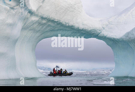 Cierva Cove, Antarktis - Dezember 23, 2016: Ein Zodiac voller Touristen durch einen Bogen in einem großen blauen Eisberg gesehen Stockfoto