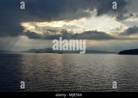 Regnerischen morgen mit dramatischen Himmel durch das Meer. Peristeres Leuchtturm auf einer kleinen Insel von Kassiopi, Korfu, Griechenland gesehen. Albanischen Küste am Horizont Stockfoto