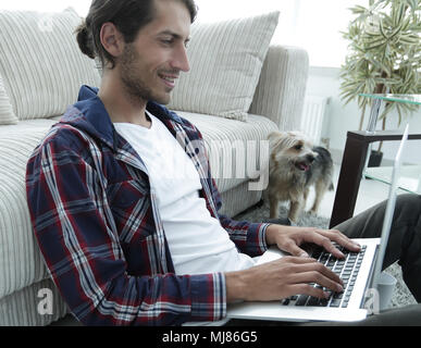 Moderne Kerl mit einem Laptop auf den Boden neben das Sofa Stockfoto