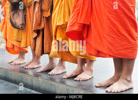 Low Angle View der Gruppe der Barefoot Männer tragen orangefarbene Gewänder nebeneinander auf einem Gehsteig. Stockfoto