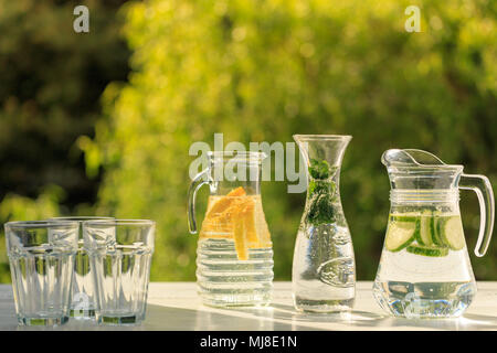 Drei Varianten von frischen, hausgemachten Limonade mit Zitrone, Gurke und Minze. Limonade in Krüge und Karaffen auf Garten. Stockfoto