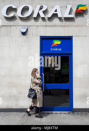 Eine Frau außerhalb der hinteren Eingang des Coral Wettbüro auf Warren Street, London, NW1, England warten Stockfoto