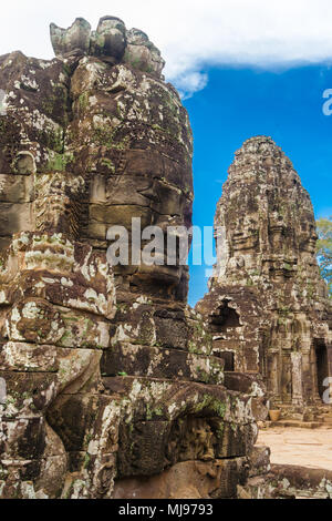 Eine monumentale steinerne Gesicht des berühmten Bayon Tempel in Angkor, Kambodscha. Im Hintergrund, ein weiterer Turm mit zwei Gesicht Skulpturen gesehen werden kann. Stockfoto