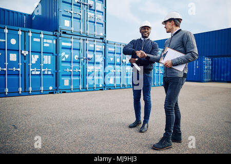 Zwei zusammen lächeln Ingenieure tragen hardhats Hände schütteln im Stehen durch den Versand von Behältern in einem Güterbahnhof Stockfoto