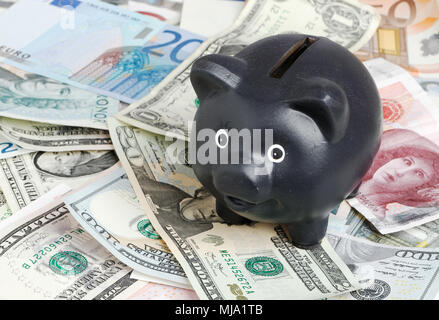Schwarz Sparschwein auf einem Stapel von Banknoten unterschiedlicher Stückelung und Währungen. Stockfoto