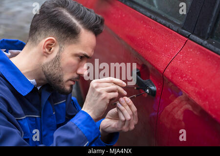 Junger Mann Öffnen rotes Auto Tür mit Lockpicker Stockfoto