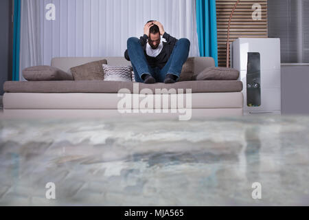 Mann auf Sofa mit Hände auf den Kopf Umkippen in Zimmer überflutet mit Wasser Stockfoto