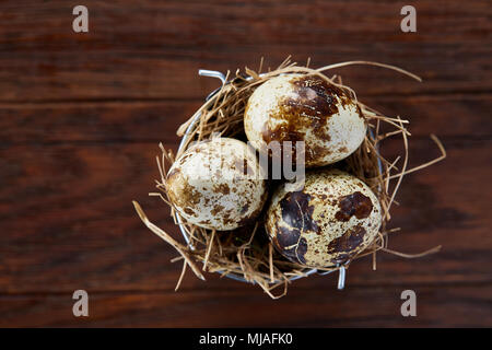 Drei frische rohe beschmutzt Wachteleier im Heu Nest auf dunklem Hintergrund, Nahaufnahme, selektive konzentrieren. Einige kopieren Platz für Ihren Text. Dekorative ländlichen Stockfoto