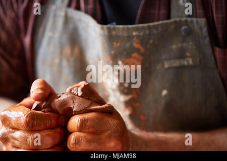 Flache Tiefenschärfe close-up Hände eines männlichen Potter in Plaid Shirt und schmutzigen Schürze Ton angeschlagen, selektiver Fokus, Nahaufnahme. Kreative Arbeit Prozess Stockfoto
