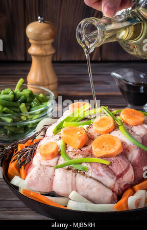 Rohes Schweinefleisch chop Fleisch Rolle aufgewickelt mit Garn Jute gießen Olivenöl mariniert mit grobem Meersalz Pfeffer verschiedene Gemüse mit Karotten, grüne Zwiebeln auf Stockfoto