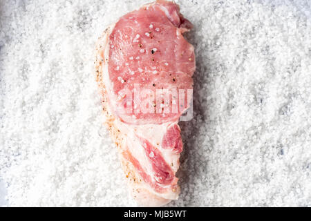 Slice Steaks rohes Schweinefleisch Chop mariniertes Fleisch auf dem Hintergrund von grobem Meersalz vorbereitet zum Backen Salzen ruckartig Stockfoto