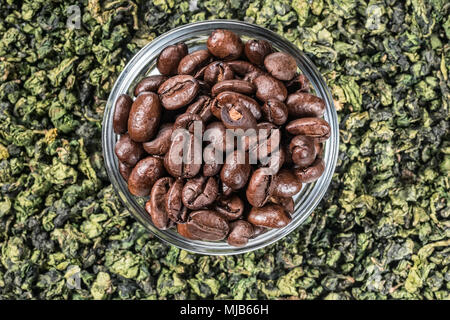 Korn frisch gerösteten Kaffee in der Schüssel im grünen Tee Blätter asiatischen Hintergrund. Essen Konzept Getränk der Wahl für Health Ingredients Kaffee coffea Stockfoto