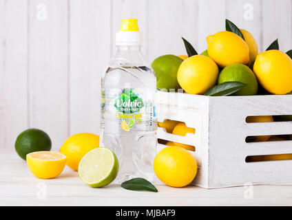 LONDON, Großbritannien - 12 April 2017: Kunststoff Flasche Volvic noch Wasser auf Holz- Hintergrund mit Zitronen und Limetten in Weiß Holzkiste. Stockfoto