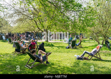 Die Menschen essen und trinken Kaffee draußen, während das warme Wetter im Frühling in einem wunderschönen Obstgarten genießen Im Orchard Tea Garden ein beliebter Veranstaltungsort i Stockfoto