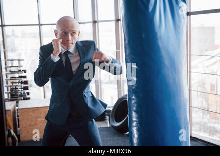 Eine verärgerte kahlen Geschäftsmann schlägt ein Boxing Birne in der Turnhalle. Konzept der Anger Management. Stockfoto