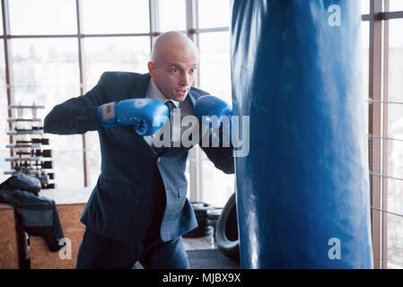 Eine verärgerte kahlen Geschäftsmann schlägt ein Boxing Birne in der Turnhalle. Konzept der Anger Management. Stockfoto