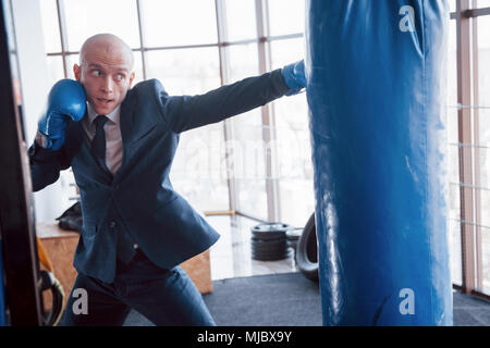 Eine verärgerte kahlen Geschäftsmann schlägt ein Boxing Birne in der Turnhalle. Konzept der Anger Management. Stockfoto