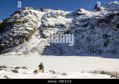 Ein Wanderer geniesst den Blick auf die schneebedeckten Berge und der zugefrorene See vor ihm. Melu, Korsika, Frankreich. Stockfoto