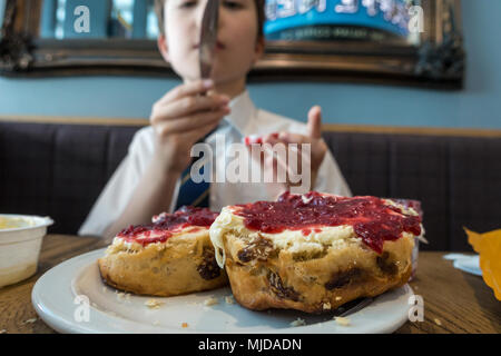 Ein Junge mit einem Obst scone mit Clotted Cream und Himbeermarmelade gekrönt. Stockfoto