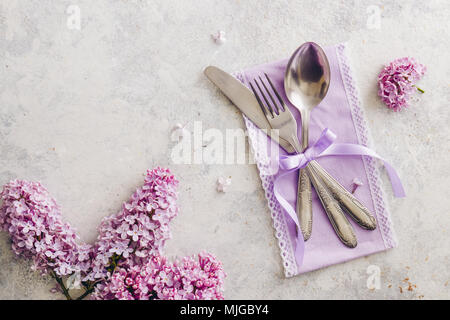 Frühling Tischdekoration mit lila Blüten. Elegante Tischdekoration mit lila Blüten, violett serviette und vintage Besteck auf rustikalen Hintergrund. Stockfoto