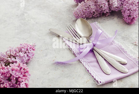 Frühling Tischdekoration mit lila Blüten. Elegante Tischdekoration mit lila Blüten, violett serviette und vintage Besteck auf rustikalen Hintergrund. Stockfoto