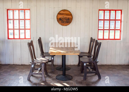 Alten hölzernen Tisch und Stühle schmücken im Restaurant mit rotem Fenster auf die weiße Wand im Hintergrund. Stockfoto