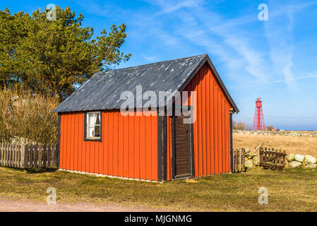 Kapelludden auf Oland, Schweden. Verwitterte rot Holz in Küstenlandschaft Schuppen mit roter Leuchtturm im Hintergrund. Stockfoto