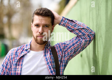 Attraktiven jungen Mann, der im städtischen Hintergrund. Kerl suchen Bei camera legere Kleidung. Lifestyle Konzept. Stockfoto